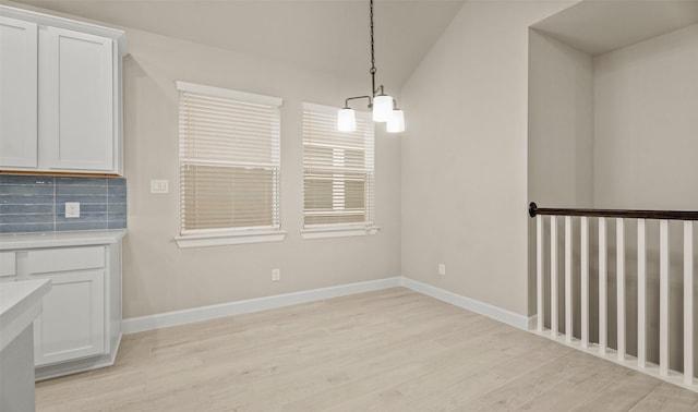 unfurnished dining area with a chandelier, light wood-style flooring, and baseboards