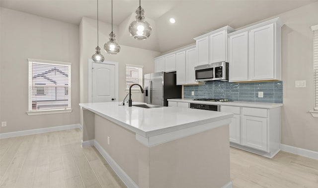 kitchen with a kitchen island with sink, a sink, stainless steel appliances, white cabinets, and backsplash