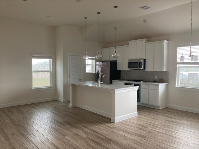 13109 Mundet Dr, Houston, TX 77047 - kitchen featuring stainless steel appliances, white cabinetry, backsplash, light wood-style floors, and pendant lighting