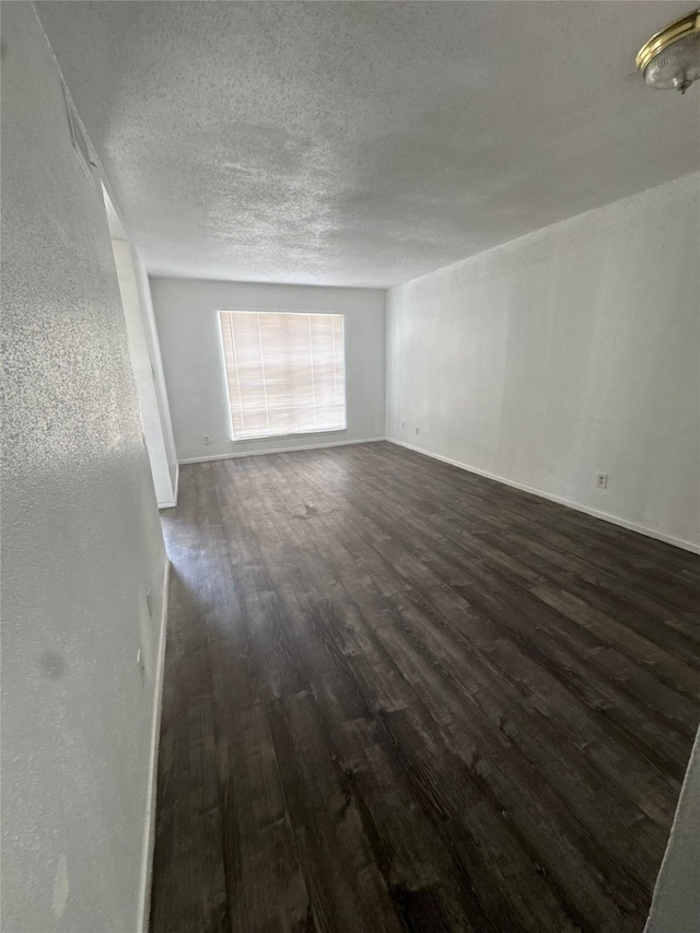 unfurnished room with dark wood-style floors, a textured ceiling, and baseboards