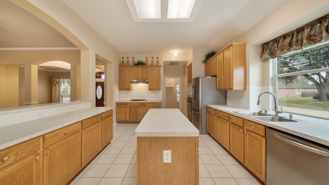 kitchen with a kitchen island, under cabinet range hood, light tile patterned floors, appliances with stainless steel finishes, and a sink