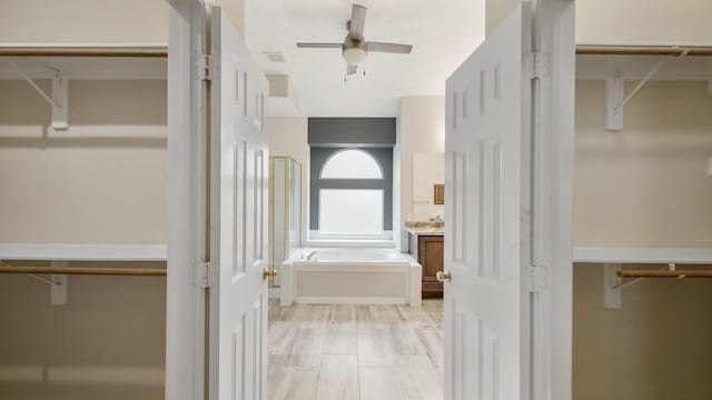 bathroom featuring vanity, wood finished floors, ceiling fan, a spacious closet, and a garden tub