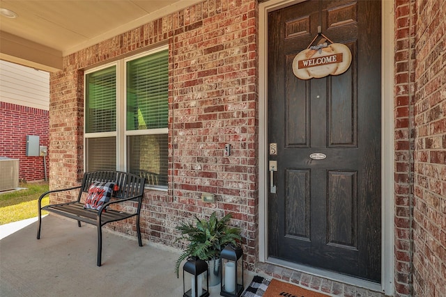 doorway to property featuring central air condition unit, brick siding, and a porch