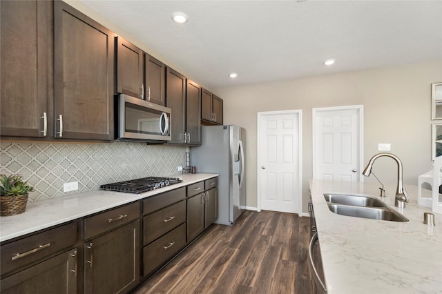 kitchen with a sink, backsplash, stainless steel appliances, dark brown cabinets, and dark wood-style flooring