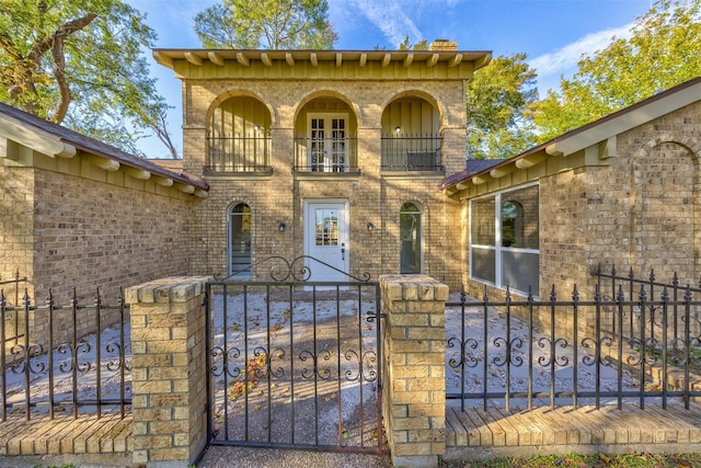 entrance to property with brick siding, a gate, a balcony, and fence