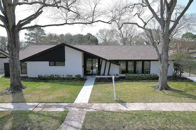 mid-century modern home with brick siding, a shingled roof, and a front yard