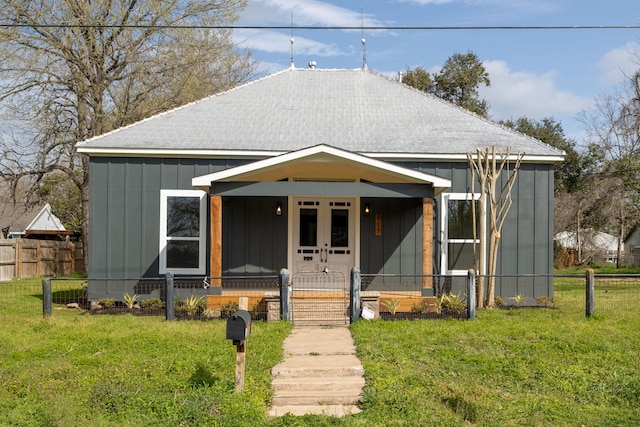 bungalow featuring a front lawn, fence, french doors, roof with shingles, and board and batten siding