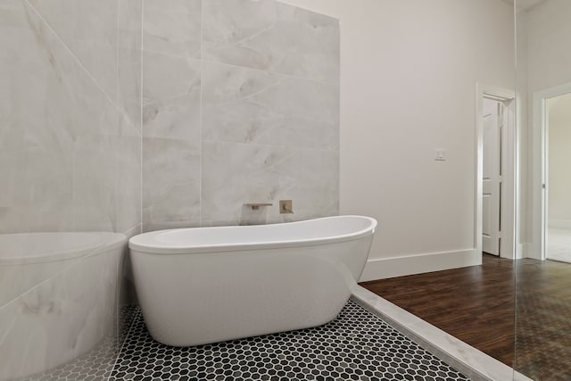 bathroom featuring a freestanding tub, baseboards, tile walls, and wood finished floors