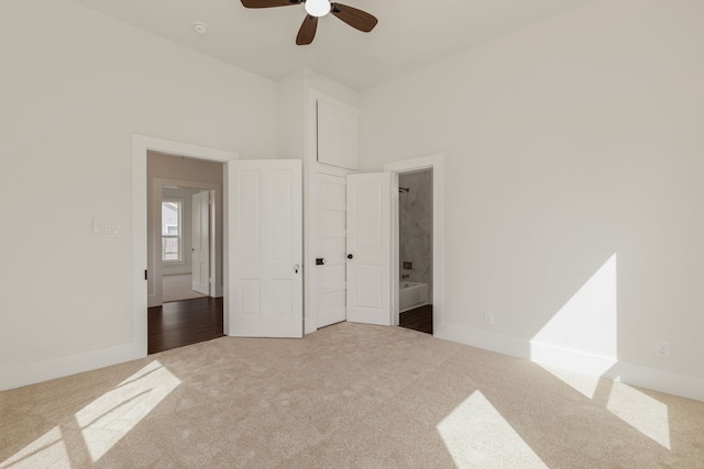 unfurnished bedroom with ensuite bath, a towering ceiling, carpet flooring, baseboards, and ceiling fan