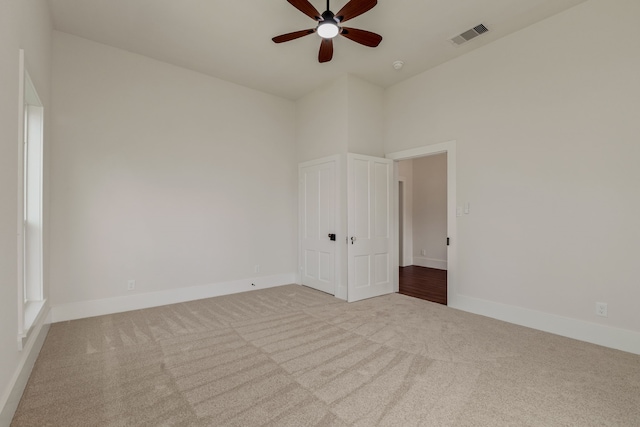 empty room featuring visible vents, a ceiling fan, a high ceiling, carpet flooring, and baseboards