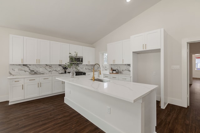 kitchen featuring an island with sink, a sink, vaulted ceiling, white cabinetry, and stainless steel microwave