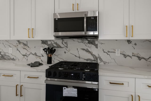 kitchen featuring gas stove, light stone countertops, white cabinets, stainless steel microwave, and tasteful backsplash