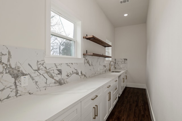 bar featuring visible vents, backsplash, baseboards, dark wood-style flooring, and a sink