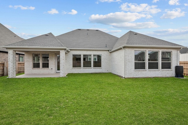 rear view of house with a patio area, a lawn, roof with shingles, and fence