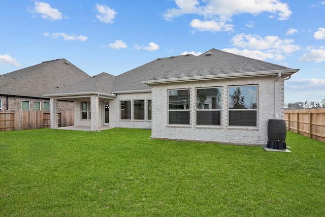 rear view of property with a patio area, a yard, a fenced backyard, and a shingled roof