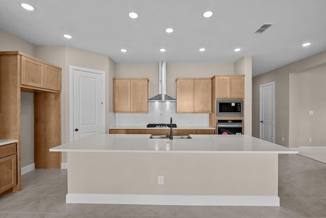 kitchen with a center island with sink, built in microwave, a sink, stainless steel oven, and wall chimney exhaust hood