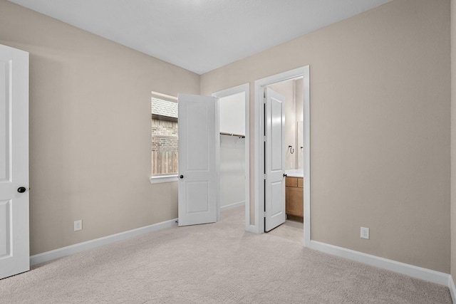 unfurnished bedroom featuring light colored carpet, connected bathroom, a walk in closet, and baseboards