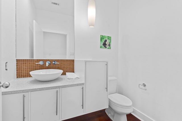 bathroom with visible vents, toilet, wood finished floors, decorative backsplash, and vanity