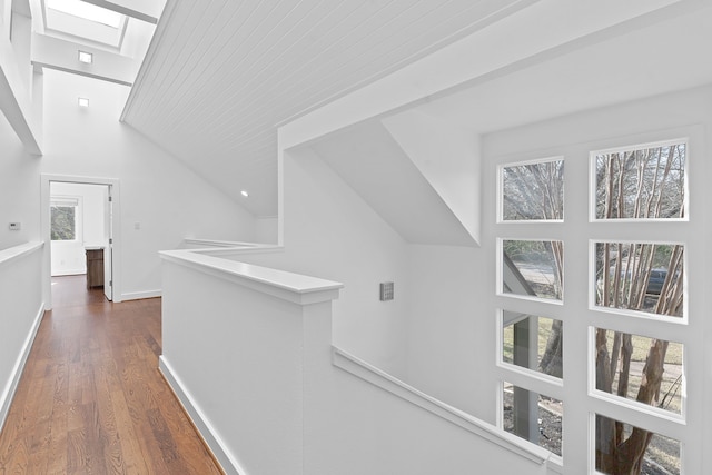 hallway with dark wood-type flooring, vaulted ceiling with skylight, an upstairs landing, and baseboards