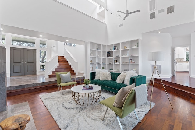 living room with visible vents, stairs, a high ceiling, and wood finished floors