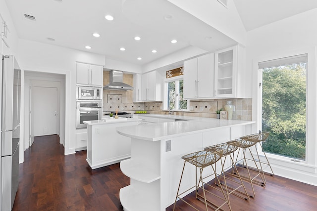 kitchen featuring visible vents, backsplash, wall chimney range hood, appliances with stainless steel finishes, and a peninsula