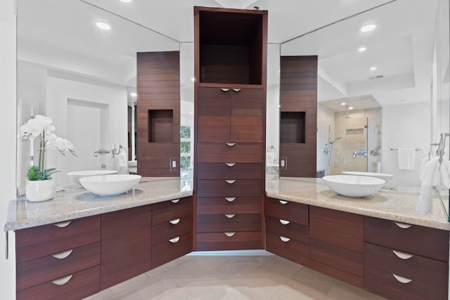 full bath featuring visible vents, a stall shower, two vanities, and a sink