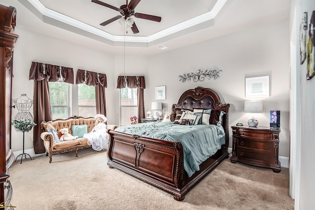 carpeted bedroom featuring a tray ceiling, a ceiling fan, visible vents, and crown molding