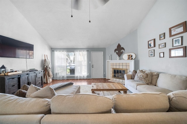 living room with a textured ceiling, wood finished floors, vaulted ceiling, and a tile fireplace