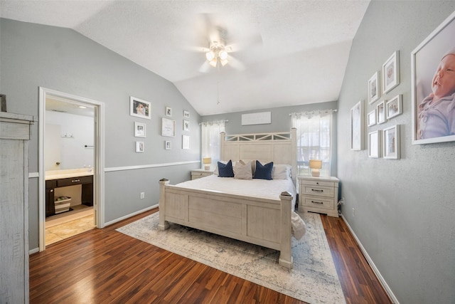 bedroom with dark wood-style floors, ensuite bath, baseboards, and vaulted ceiling