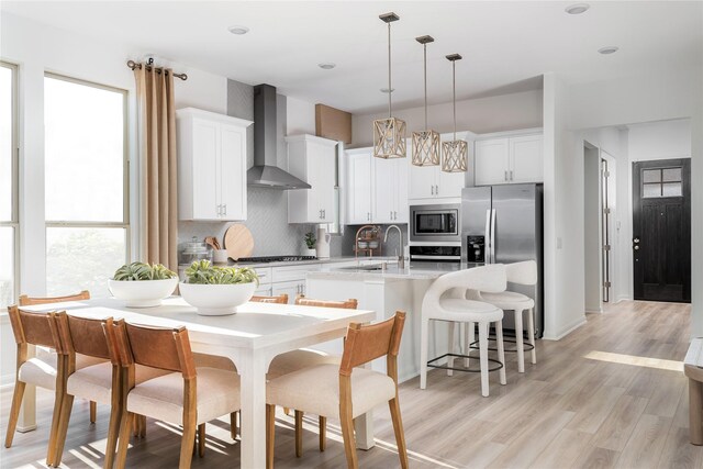 26711 Grandiflora Dr, Magnolia, TX 77355 - kitchen featuring wall chimney range hood, stainless steel appliances, a center island with sink, backsplash, and light wood finished floors