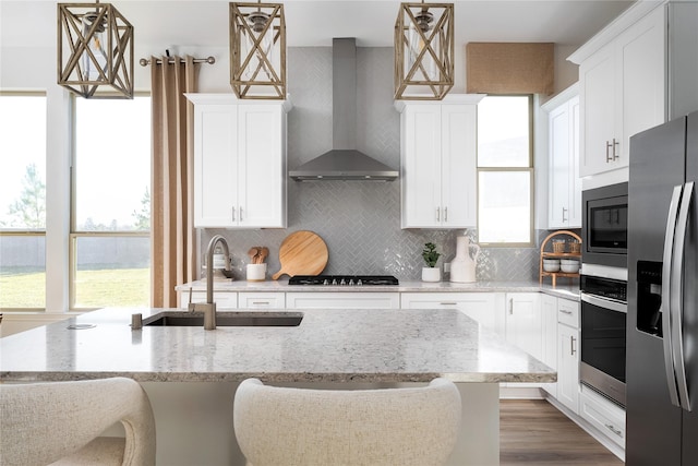 kitchen with a sink, white cabinets, appliances with stainless steel finishes, wall chimney range hood, and backsplash