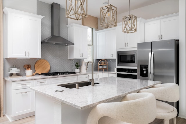 kitchen with a sink, backsplash, white cabinetry, appliances with stainless steel finishes, and wall chimney range hood