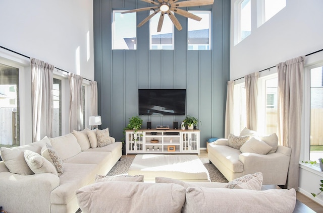 living area with wood finished floors, baseboards, a towering ceiling, and ceiling fan