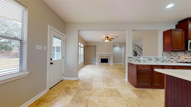 kitchen featuring a ceiling fan, plenty of natural light, a fireplace, light countertops, and tasteful backsplash