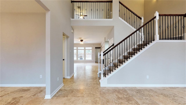 foyer entrance featuring stairs, a high ceiling, baseboards, and a ceiling fan