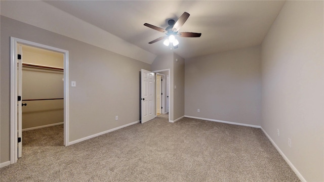 unfurnished bedroom with a spacious closet, baseboards, vaulted ceiling, carpet flooring, and a ceiling fan