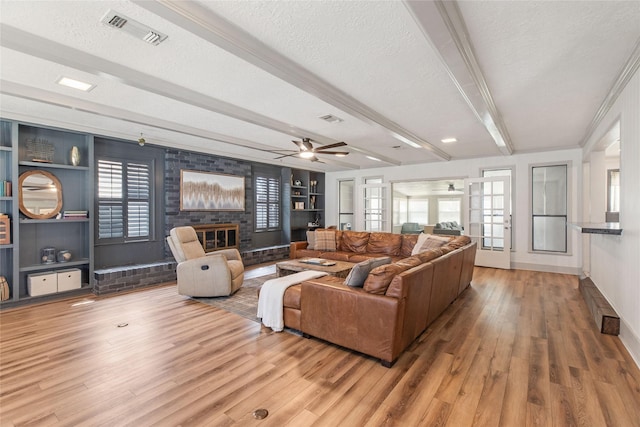 living room featuring beamed ceiling, a textured ceiling, visible vents, and wood finished floors