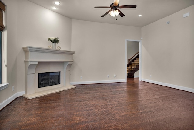 unfurnished living room with a glass covered fireplace, stairway, baseboards, and ceiling fan