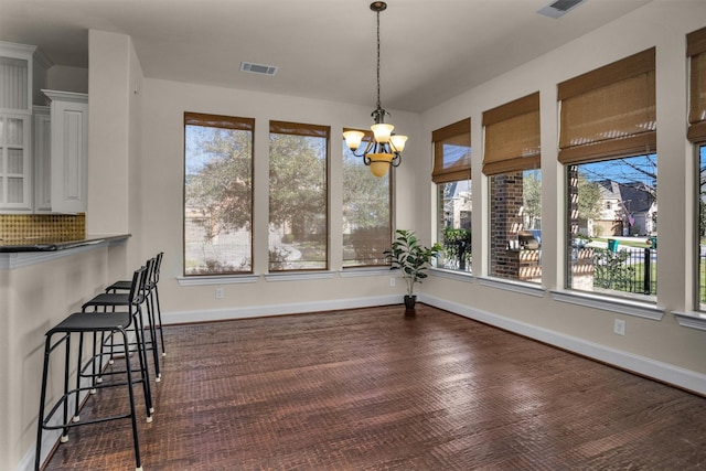 unfurnished dining area featuring visible vents, baseboards, a notable chandelier, and dark wood-type flooring