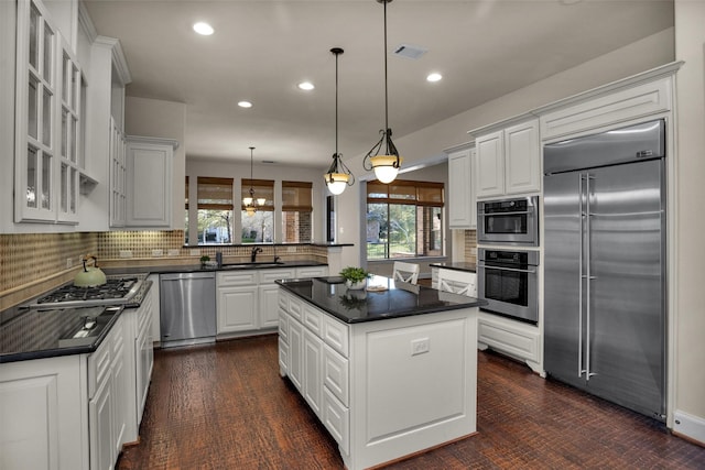 kitchen featuring a sink, stainless steel appliances, white cabinetry, dark countertops, and a center island