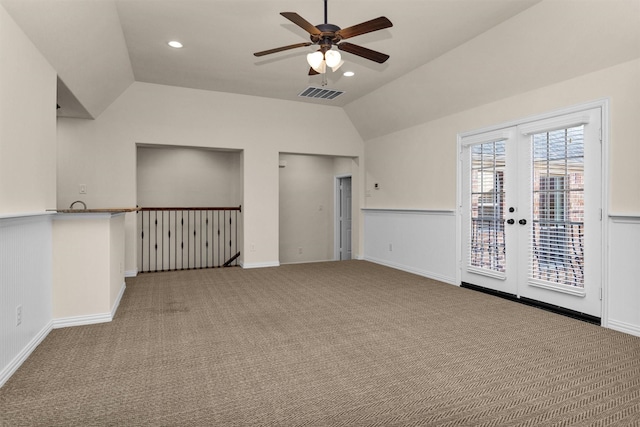 carpeted spare room with visible vents, ceiling fan, a wainscoted wall, lofted ceiling, and french doors