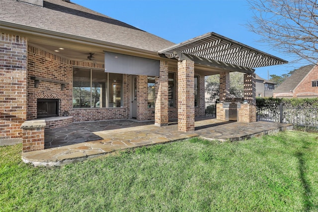 rear view of property featuring brick siding, an outdoor brick fireplace, fence, a ceiling fan, and a patio