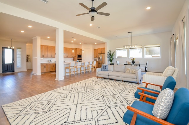 living area with recessed lighting, light wood-style flooring, and ceiling fan with notable chandelier