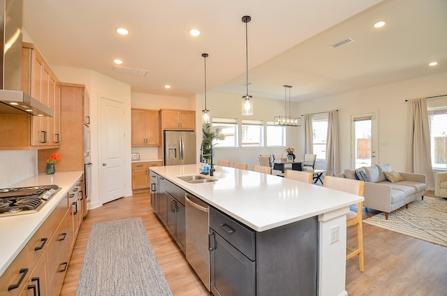 kitchen with a breakfast bar, light brown cabinetry, a sink, appliances with stainless steel finishes, and wall chimney exhaust hood