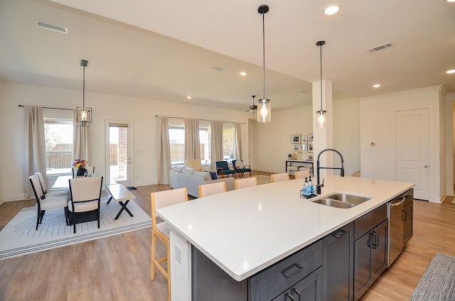 kitchen with light wood finished floors, visible vents, a sink, light countertops, and a kitchen island with sink