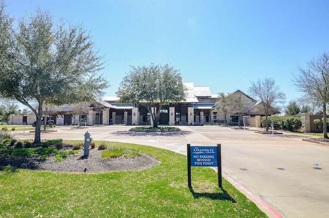 view of front of house featuring stone siding, curved driveway, and a front yard