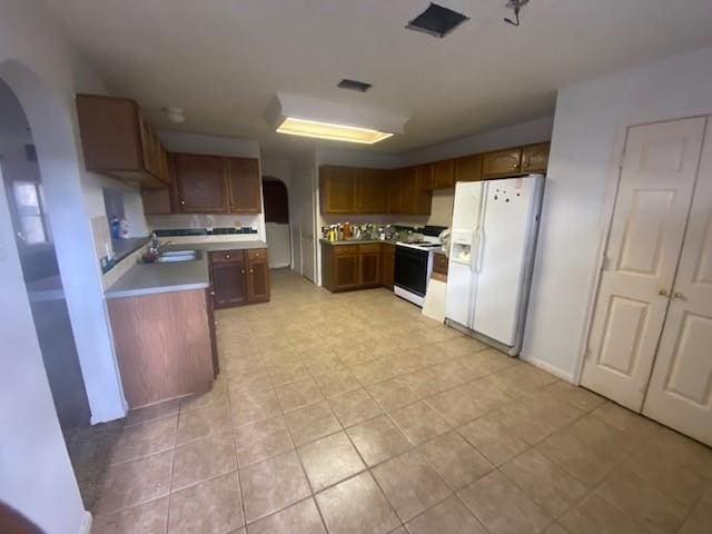 kitchen with arched walkways, a sink, white refrigerator with ice dispenser, range with electric stovetop, and brown cabinets