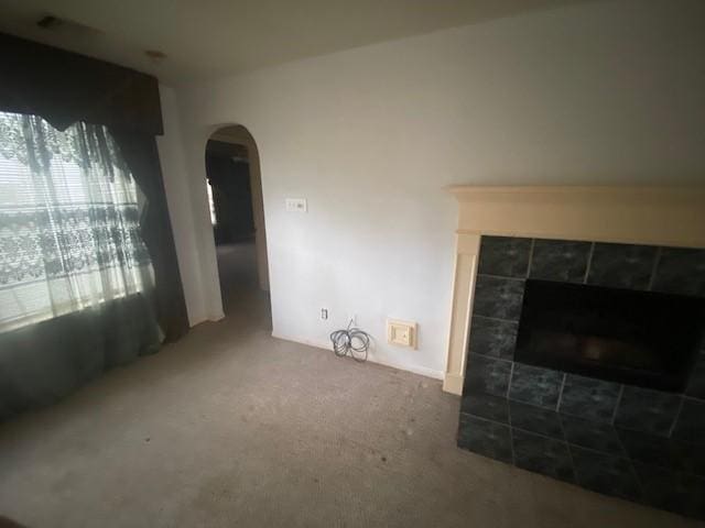 living room with a tiled fireplace, carpet, and arched walkways