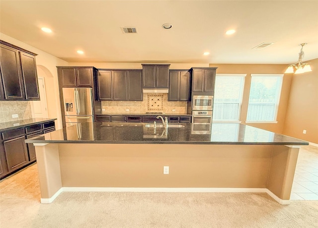 kitchen with visible vents, a sink, a spacious island, appliances with stainless steel finishes, and dark brown cabinets