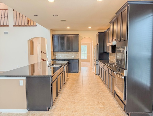 kitchen featuring a center island with sink, arched walkways, appliances with stainless steel finishes, and a sink